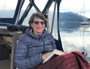 Connie on a boat, smiling with a book in her lap and the mountains in the background.