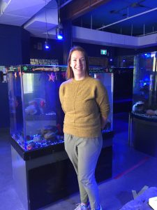NSMEC Curator Jenny Wright stands infront of a fish tank at the aquarium.